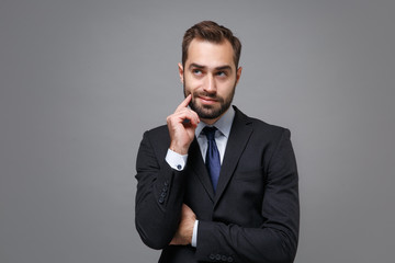 Pensive young business man in classic black suit shirt tie posing isolated on grey background studio portrait. Achievement career wealth business concept. Mock up copy space. Put hand prop up on chin.