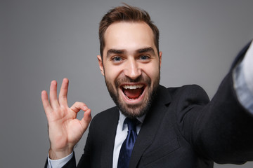 Close up of business man in suit shirt tie posing isolated on grey background. Achievement career wealth business concept. Mock up copy space. Doing selfie shot on mobile phone, showing OK gesture.