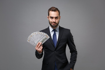 Confident young business man in classic suit shirt tie posing isolated on grey background. Achievement career wealth business concept. Mock up copy space. Hold fan of cash money in dollar banknotes.