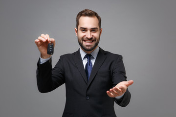 Smiling business man in classic black suit shirt tie posing isolated on grey background. Achievement career wealth business concept. Mock up copy space. Stand with otstretched hand, holding car keys.