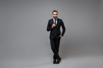 Fototapeta na wymiar Smiling young bearded business man in classic black suit shirt tie posing isolated on grey background studio portrait. Achievement career wealth business concept. Mock up copy space. Looking camera.