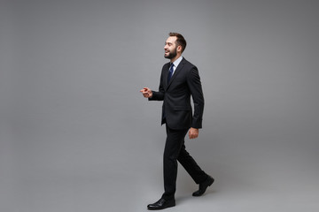 Fototapeta na wymiar Side view of cheerful young bearded business man in classic black suit shirt tie posing isolated on grey wall background. Achievement career wealth business concept. Mock up copy space. Looking aside.
