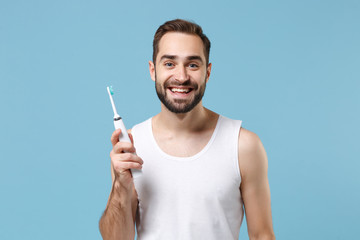 Bearded young man 20s years old in white shirt hold choice electric brushes isolated on blue pastel...