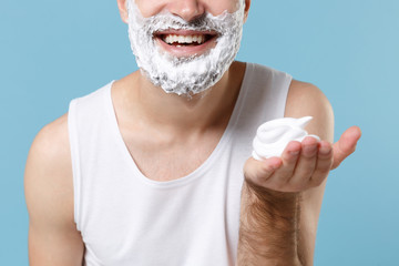 Close up cropped of bearded man in white shirt face covered with shaving foam isolated on blue...