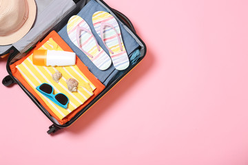 Open suitcase with beach accessories on pink background, top view. Space for text