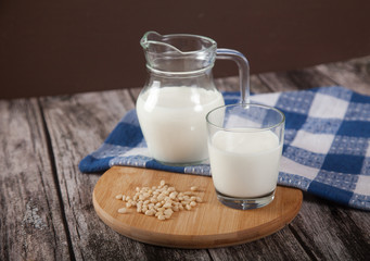Vegetarian pine nut milk in a glass cup and jug, on a wooden stand with a blue linen napkin.