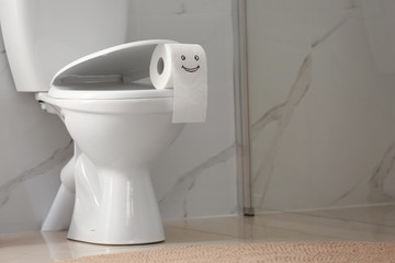 Roll of paper with funny face on toilet bowl in bathroom