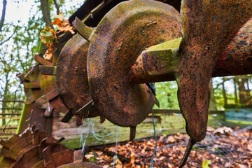 Detailed view of an old rusty harrow standing unused on a storage place in the forest.
