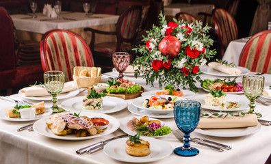 Served for holiday banquet restaurant table with dishes, snack, salads, cutlery, wine and water glasses. European food in a restaurant setting. Table set for an event party. catering
