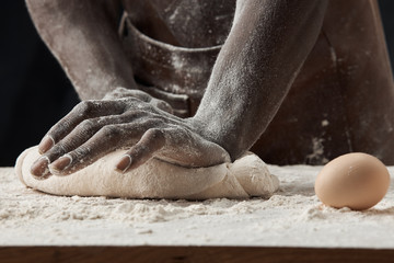 hands of a black man kneading the dough on the table with eggs and flour