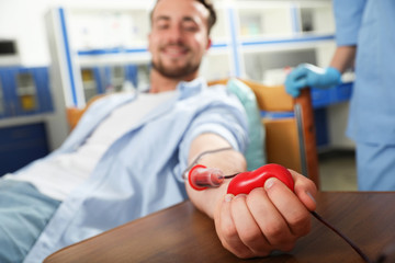 Young man making blood donation in hospital, focus on hand - obrazy, fototapety, plakaty