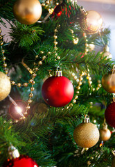 red christmas ball hanging on green pine with red and gold ornaments and lights