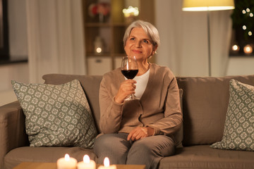 people, alcohol and drinks concept - happy senior woman drinking red wine from glass at home in...