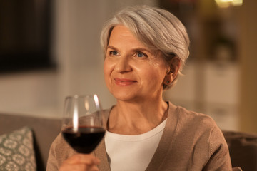 people, alcohol and drinks concept - happy senior woman drinking red wine from glass at home in evening