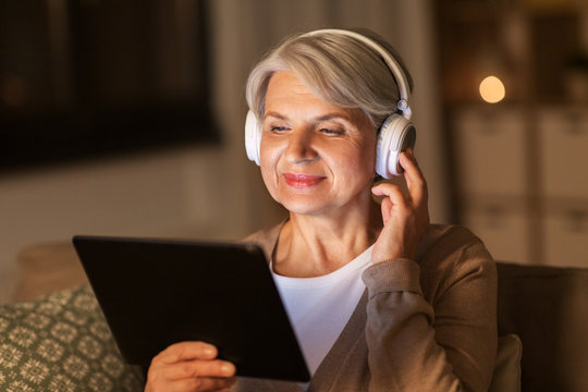 technology, people and lifestyle concept - happy senior woman in headphones and tablet pc computer listening to music at home in evening