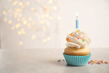 Birthday cupcake with candle on light grey table against blurred lights. Space for text