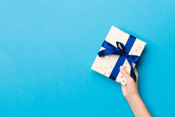 Woman arms holding gift box with colored ribbon on blue table background, top view and copy space...