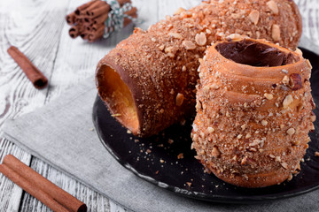 Trdelnik covered in nuts and sugar with chocolate inside against white wooden background. Czech street food