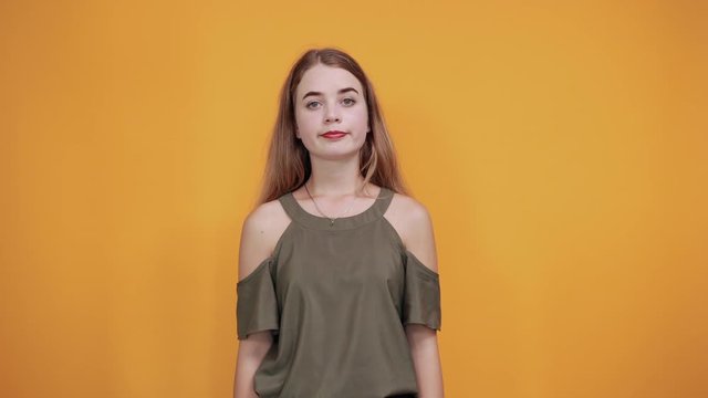 Caucasian attractive girl over orange wall making unimportant gesture while lifting the shoulders wearing haki shirt