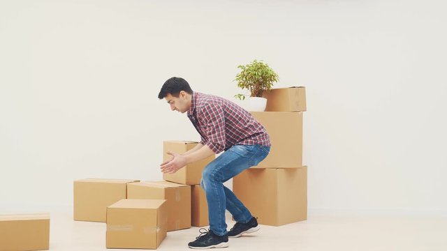 Handsome young man carrying carton boxes, stumbling over something, dropping boxes, looking perplexed.