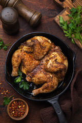 whole fried chicken tabaka on cast iron pan, old wooden background