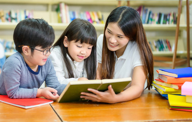 A Group of Asian Student Kid Reading a book with women teacher in School library with Shelf of Books in Background, Asian Kid Education Concept - 304708933