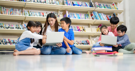 Group of Asian Student Kid Learning to use Laptop in Library with Women Teacher, Shelf of Books in Background, Asian Student Education Concept - 304709374