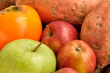 Colorful background with healthy fruits and vegetables like apples, kaki and sweet potatoes lying close together.