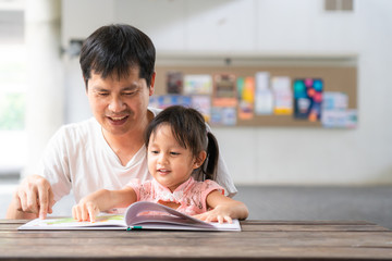 Asian father and daughter are reading the storybook together and they are smiling with happy...