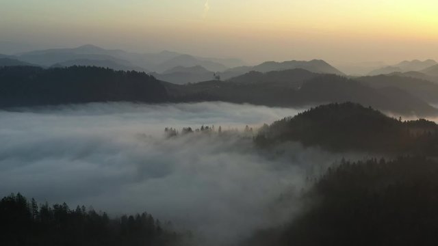 Flying over fog filled valley at sunrise in Slovenia as hilltops and mountains peak out of the clouds.