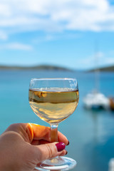 hand with glass of white wine served outside on balcony with sea view