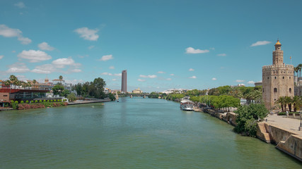 Fototapeta na wymiar Views of the city from the bridge Puente San Telmo over Guadalquivir river towards watchtower Torre del Oro, Triana bridge and neighborhood and Cajasol Tower, in Seville, Andalusia, Spain