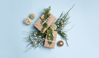 Fototapeta na wymiar Christmas gifts surrounded by gold cream pine cones, green Christmas tree foliage and delicate white flowers on a blue background. 