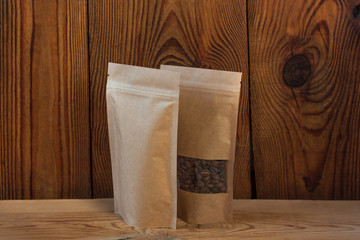Brown kraft paper pouch bags with coffee beans front view on a wooden background. Packaging for foods and goods template mock-up. Packs with clasps and windows for tea leaves and weight products.