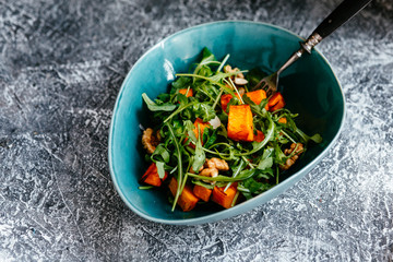 Baked pumpkin vegetarian salad with arugula and nuts in a plate on the table