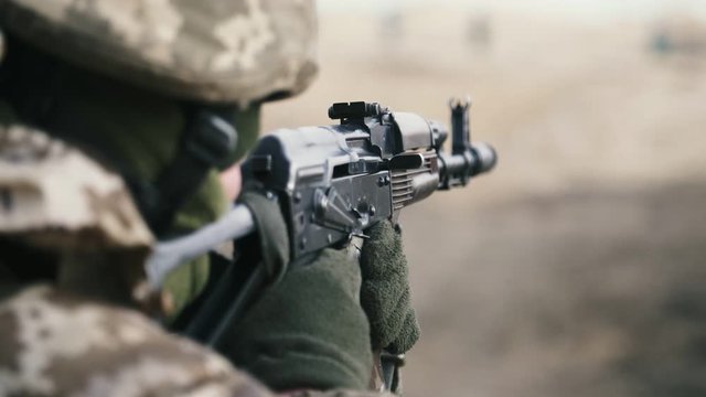 Man gunning from AK 74 in a khaki uniform in a big range in slow motion