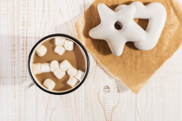 Hot Christmas drink with marshmallows in an iron mug and gingerbread cookies, on a white table.