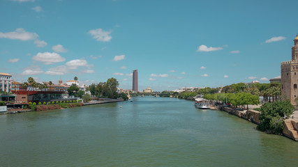 Fototapeta premium Views of the city from the bridge Puente San Telmo over Guadalquivir river towards watchtower Torre del Oro, Triana bridge and neighborhood and Cajasol Tower, in Seville, Andalusia, Spain