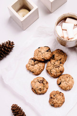 Christmas cranberry and chocolate oatmeal cookies and mug of cocoa with marshmallow on white background decorated fir cones and candles. Selective focus