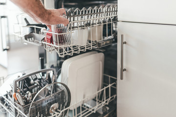 close-up of man loading or emptying dishwasher in kitchen