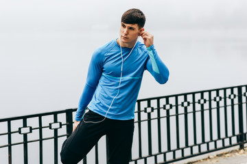 Young jogger muscular man stretching outdoor in the morning on the fog nature background. Fitness...