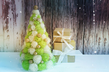 Creative Christmas tree. New Year, Christmas background, rustic style. Festive Christmas tree on white wood background and craft boxes tied with satin ribbons. Beautiful Christmas tree with Golden bal