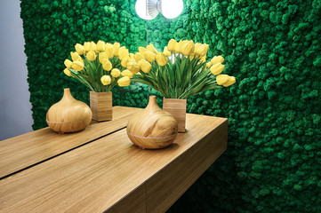 Vases and tulips on wooden cafe table. Green moss wall