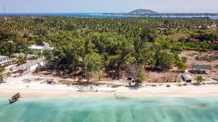 A drone shot of white sand beach on Gili Air, Lombok, Indonesia. Beautiful and clear sea water. There is a boat anchored to the beach. In the back visible Mount Rinjani. Holidays paradise.