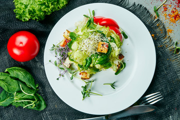 Vegetarian salad with tomatoes, tofu cheese, microgreen on a white plate. Composition with salad on a gray cloth top view. Healthy food