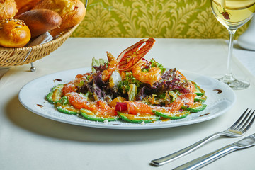 Seafood salad on a white plate with a restaurant serve. Salad with avocado, shrimp and salmon and sweet sauce. Healthy eating lifestyle.
