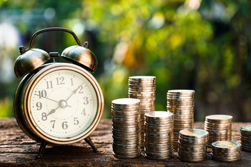 Vintage golden alarm clock with stacks of coin. Time and money for financial concept.