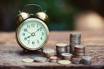 Vintage golden alarm clock with stacks of coin. Time and money for financial concept.