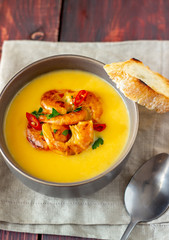 Cheese cream soup with grilled shrimp on a wooden background.