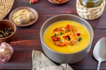 Cheese cream soup with grilled shrimp on a wooden background.